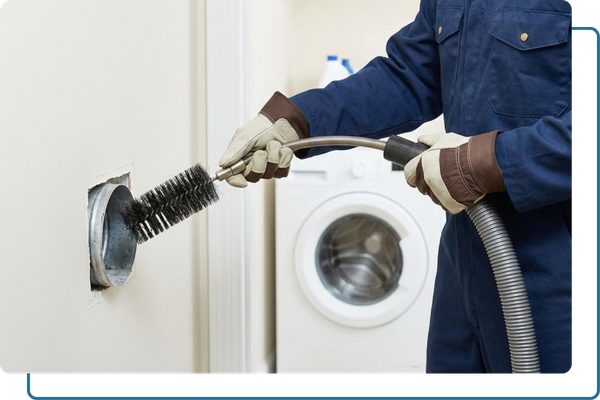 A professional technician performing routine dryer vent maintenance using a rotary brush tool on an indoor wall vent.