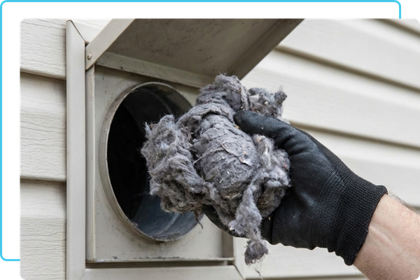 A technician's gloved hand extracting a large, dense clump of lint from an exterior dryer exhaust vent.