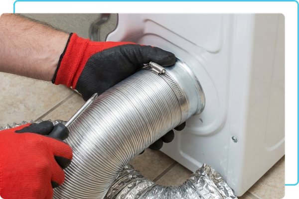 A professional wearing protective gloves carefully securing a metal transition hose to the back of a residential washing machine and dryer unit.